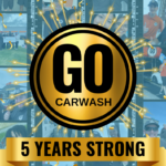 Celebratory image for GO Carwash's 5th anniversary. The image features a large gold medallion with the text "GO Carwash" in the center, surrounded by sparkling effects. Below the medallion, a gold banner reads "5 Years Strong." The background is a collage of photos showing staff and customers at various GO Carwash locations.